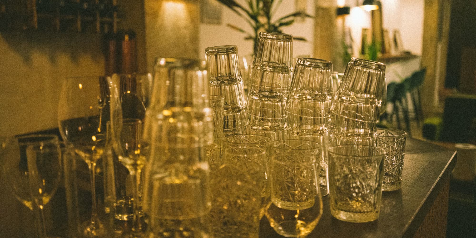 Bardisken i mörkt trä med glas på rad och två pendellampor bakom.